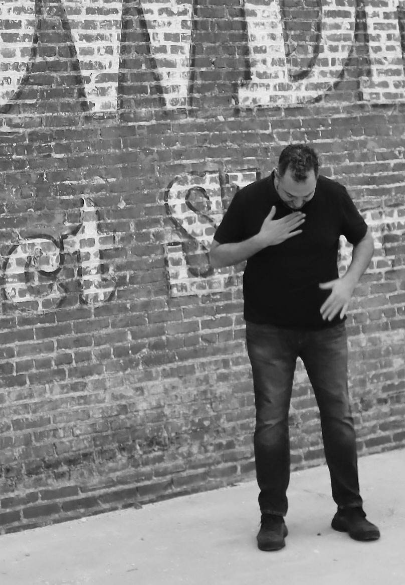 Alex Burger Portrait for Biography - Standing in front of brick painted wall