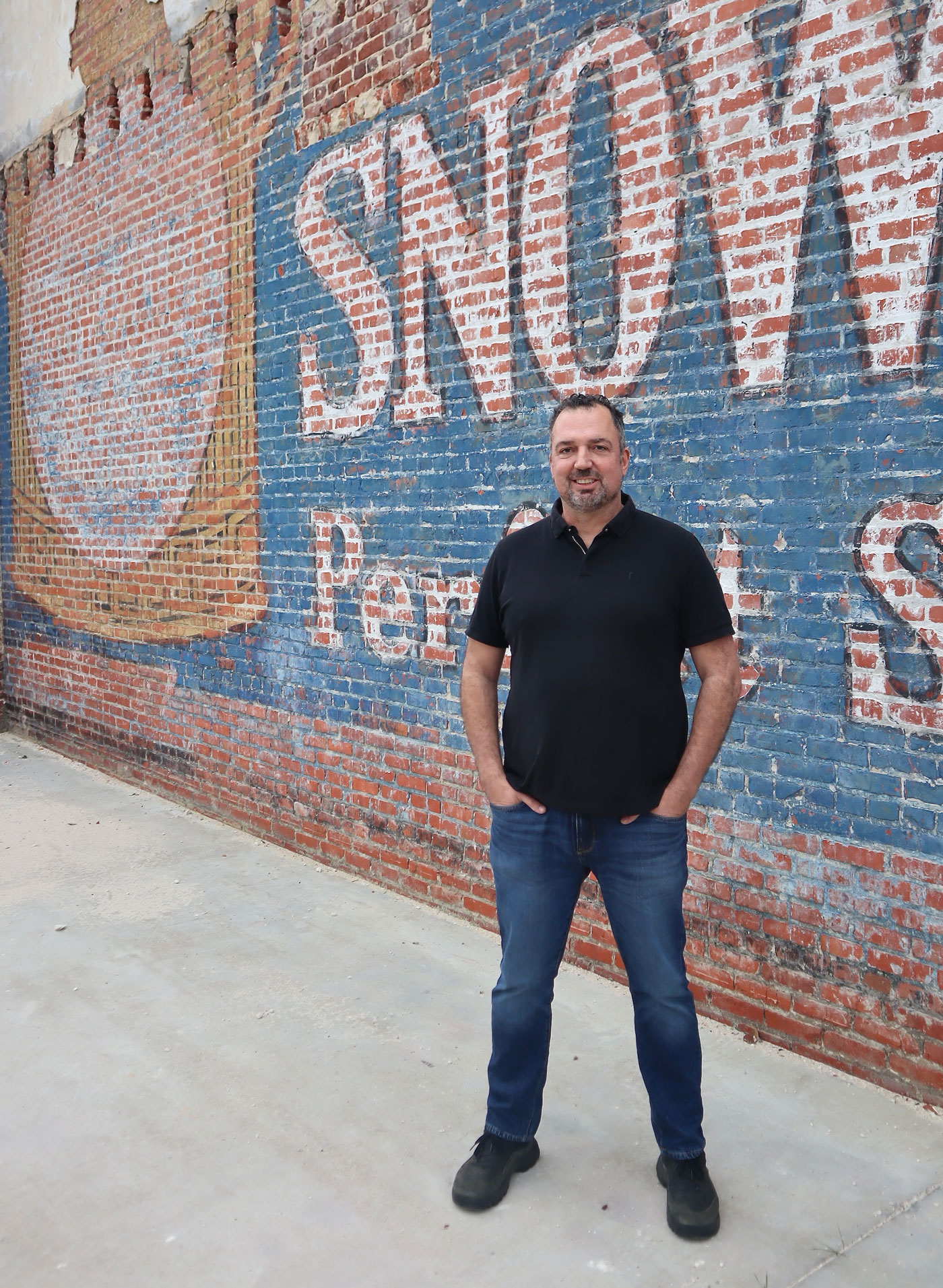 Alex Burger Portrait for Home Page - Standing in front of brick painted wall